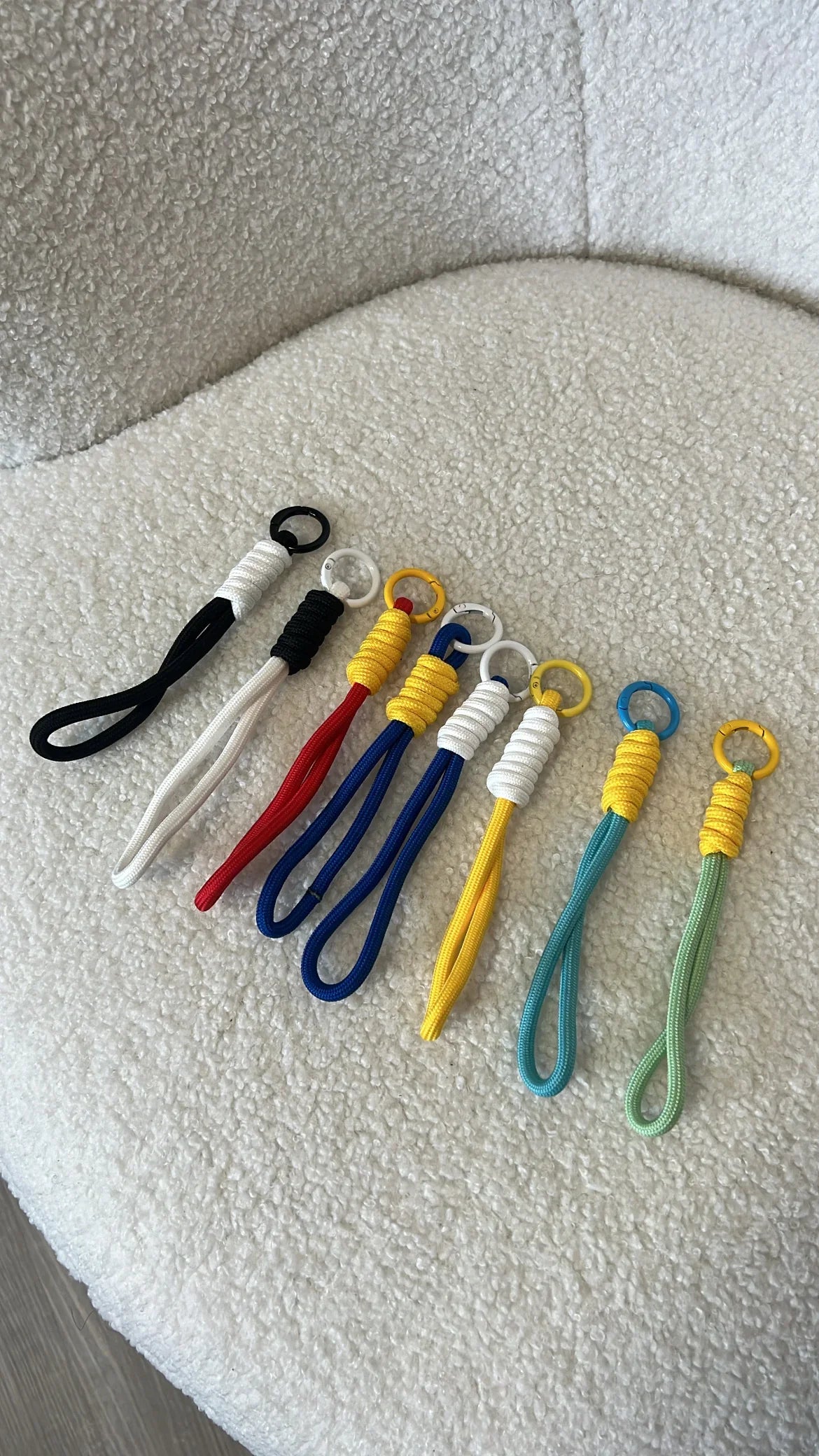 Portachiavi colorati in corda con anelli in metallo, disposti su poltrona bianca texture boucle
