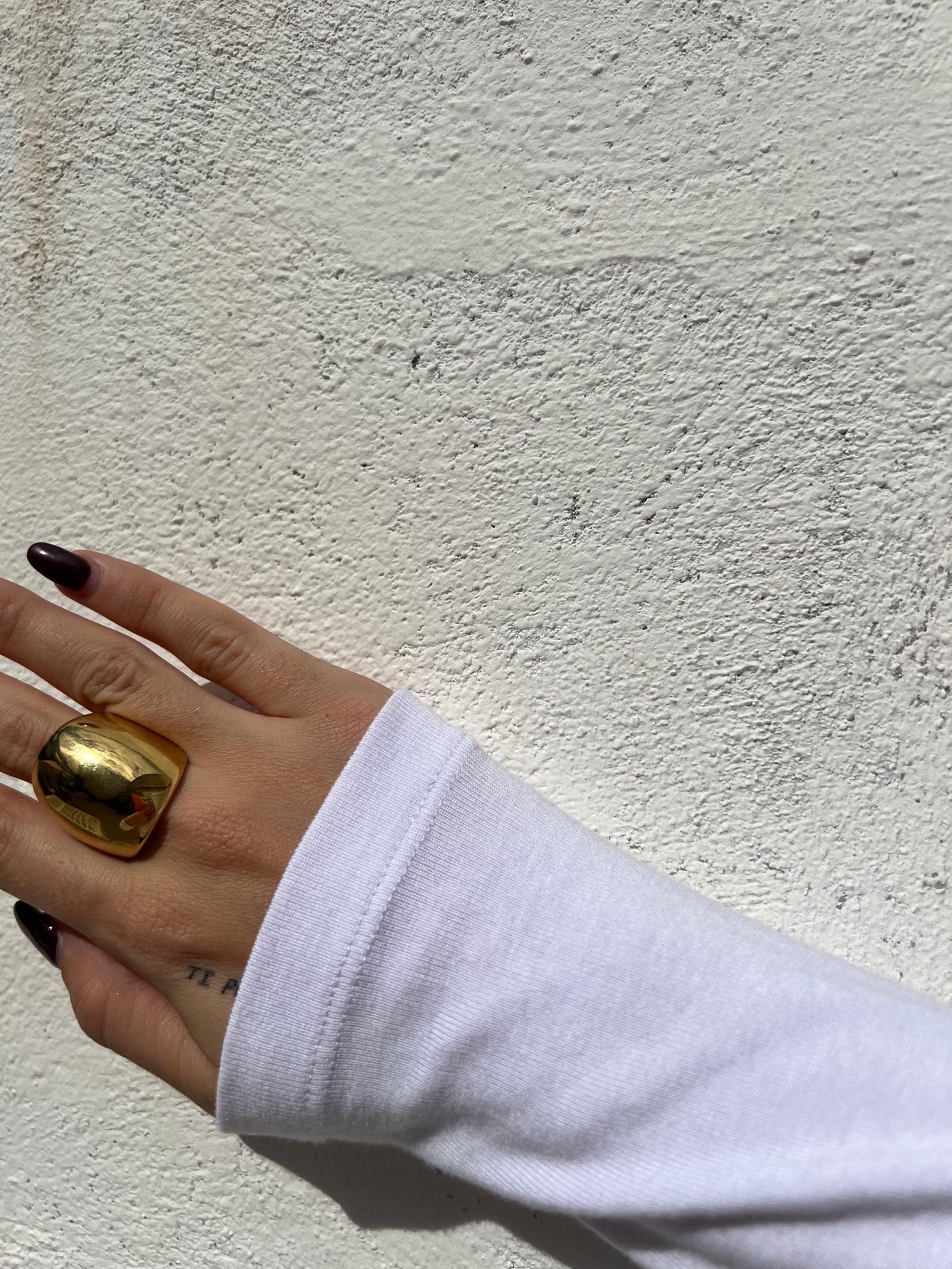 Mano femminile con un anello dorato grande e lucido su sfondo bianco, maglia bianca a manica lunga