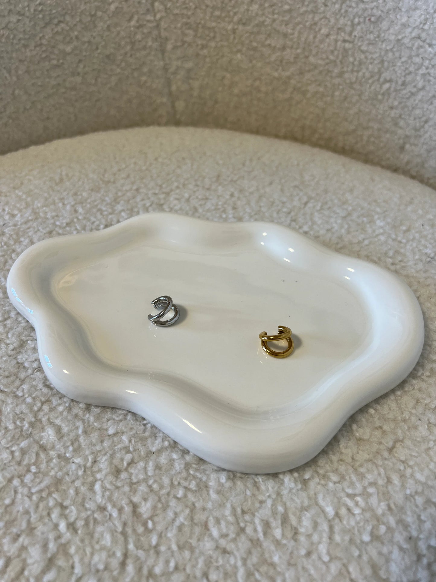 Anello doppio minimalista in argento e oro su piattino bianco ondulato, sfondo tessuto beige