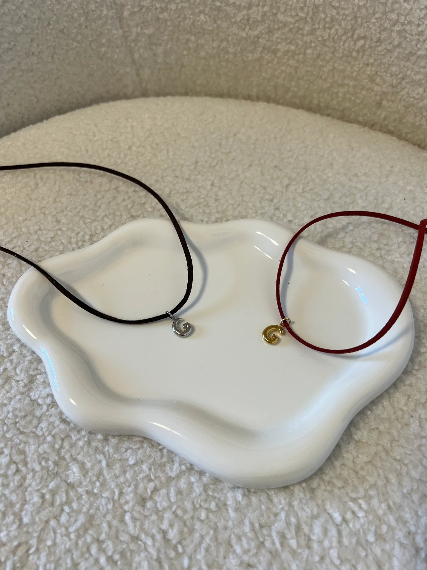 Collane minimaliste Les Soeurs 33 con ciondoli a spirale in metallo, corde nera e rossa su piatto bianco ondulato