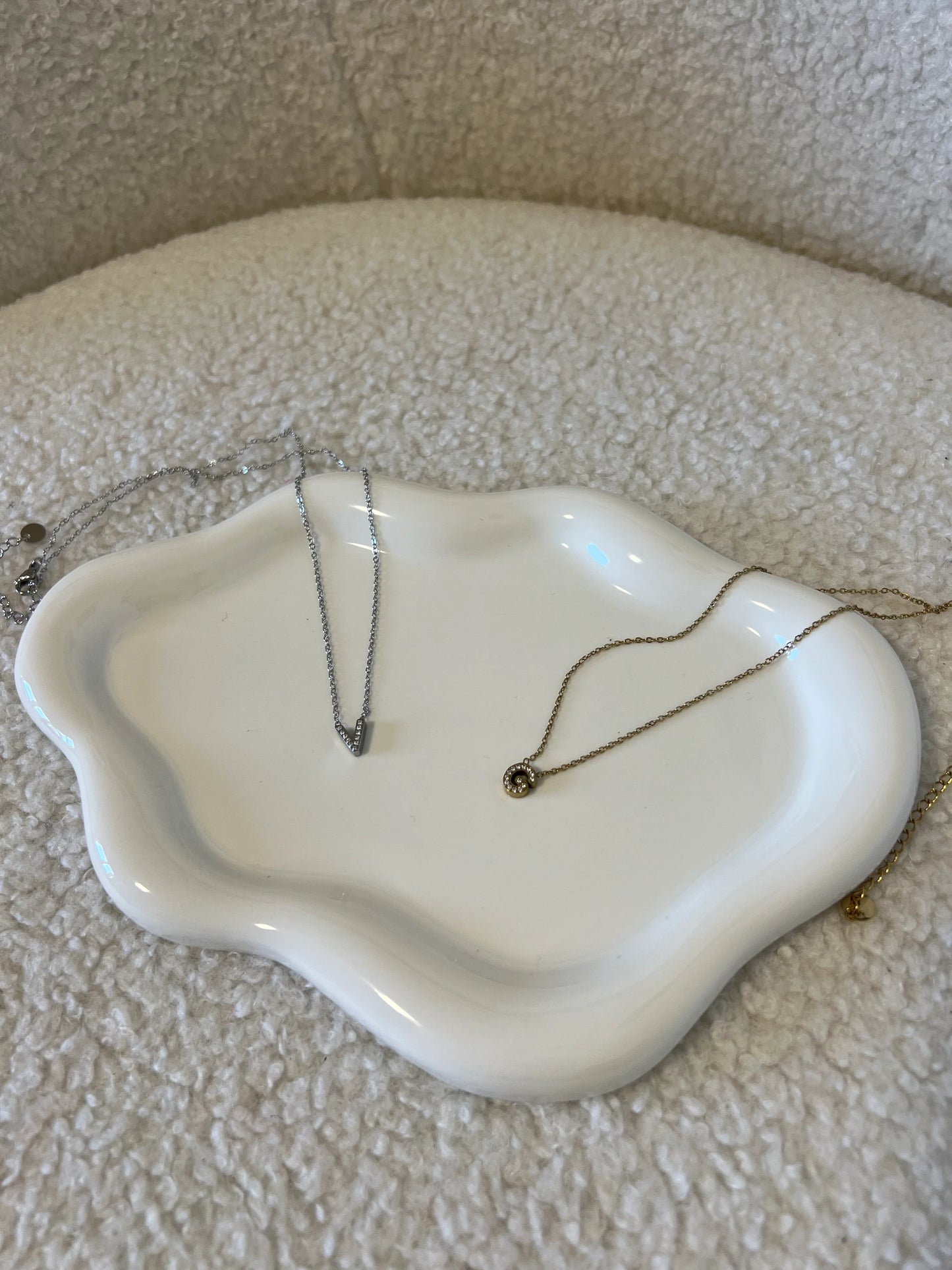 Due collane Les Soeurs 33 su piatto bianco ondulato, sfondo tessuto beige soffice